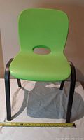 Front view of chair showing green seat, black legs, tape measure for scale