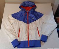 Front view of white and blue Nike windbreaker with red zippers and hood