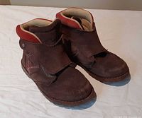Pair of brown suede UGG ankle boots front/side view showing Velcro flaps and red collar accent