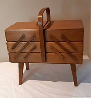 Front view of wooden cantilever sewing box with handle and legs