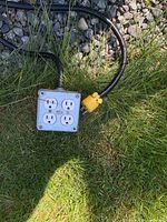 Metal quad-outlet junction box attached to black cable with yellow twist-lock plug