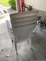Stack of white plastic patio armchairs showing backs, arms and stackable form