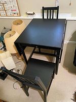 overview of black drop-leaf dining table with two matching slat-back chairs