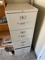 Front view of beige HON 4-drawer filing cabinet beside bookshelf
