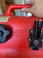 Close-up of 6.5 US gal red plastic fuel can showing capacity marking, cap, spout assembly and carry handle