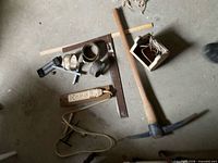All items laid out: pickaxe, carpenter square, ruler, combination square head, power strip, wooden box with cord, assorted clamps and bands