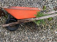 Side view of orange metal wheelbarrow showing tub, single black wheel, steel frame, wooden handles