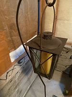 Full view of lantern hanging from curved iron support on tripod base