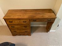 Front view of medium-brown solid wood desk showing three left drawers, one right drawer, kneehole opening, brass-tone hardware
