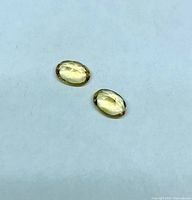 Two oval yellow faceted gemstones on light background