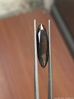 Side view of marquise smoky topaz held by tweezers showing depth and faceting