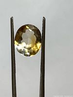Front view of oval citrine held by tweezers showing color and brilliance