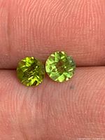 Both peridot gemstones side-by-side on fingertip showing matching size and color