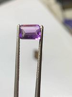 Front view of rectangular violet amethyst held by tweezers