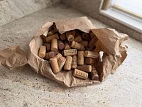 Open brown paper bag revealing a pile of used wine corks on countertop