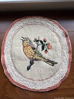 Full view of oval needlepoint showing bird motif, lace trim, pink border