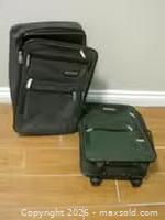 Two small softside carry-on suitcases, one black upright and one green rolling, placed on floor