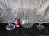 Three clear glass bowls of different styles beside soda can for scale