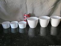 Six small white ceramic bowls next to soda can for scale