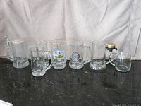 Seven glass beer mugs and steins lined on countertop