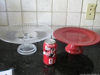 Clear glass and red pedestal cake plates side by side with soda can for scale