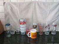 Front view of all eleven items: cocktail shaker centre, nine assorted glasses and mug aligned
