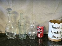 All three glass bottles and script container beside soda can for scale