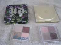 Four compacts: Urban Decay palette, YSL gold compact, two clear quad palettes