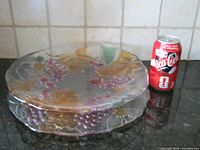 Two stacked glass pieces with grape and leaf motif beside soda can for scale