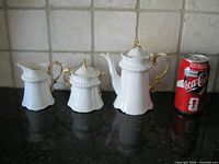 Front view of teapot, sugar bowl, creamer beside soda can for scale
