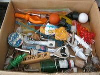 Overview of box with assorted pourers, stoppers, swizzle sticks and openers