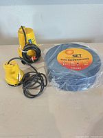 Two yellow bilge pumps with cords and sealed blue pool backwash hose