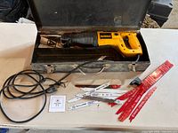 DeWalt reciprocating saw in open metal case with power cord and pile of saw blades