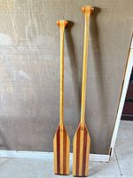 Two laminated wood canoe paddles leaning against wall