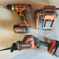 Group view of drill with battery, reciprocating saw with battery and charger