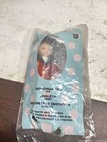 Front view of sealed polka-dot bag showing doll inside