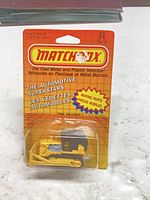 Front view of packaged Matchbox bulldozer showing vehicle color, packaging graphics, and condition
