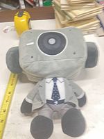 Front view of gray Sekibubi Toilet plush wearing jacket and tie next to ruler