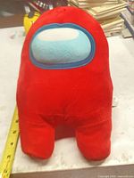 Front view of red Among Us plush beside tape measure showing height
