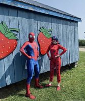 Costumed characters beside blue barn wall with strawberry art at Brooks Farms