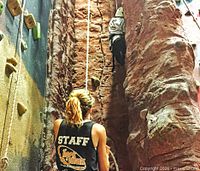 Indoor climbing wall with staff member belaying a climber