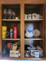 Cabinet view showing wine glasses, travel tumblers, mugs, pitcher and plates