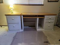 Front view of desk showing both pedestal cabinets, open center section, natural wood top, lamp on left