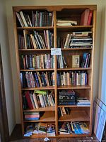Full view of tall light brown wood bookcase filled with books