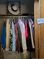 Full closet view with garments on hangers and hat on upper shelf
