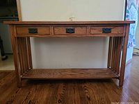 Front view of oak console table showing three drawers, slatted sides, lower shelf