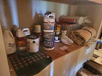 Shelf view showing multiple paint cans, cleaner jugs, drop cloths, plastic sheeting and accessory box