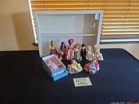 Group shot of eight dolls and display case on table