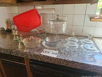 All bakeware pieces arranged on countertop: rectangular dishes, round dishes with lids, pie plates, casserole, cake stand with dome, red lid