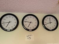 Three identical black-framed wall clocks mounted side by side